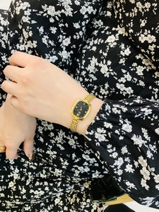 Close-up of elegant gold mesh band watch with black square dial on model's wrist