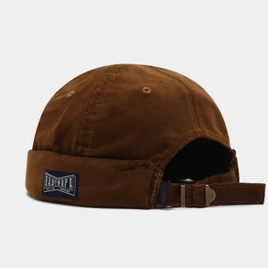 Detail of brown corduroy skull cap featuring adjustable metal buckle and blue woven label