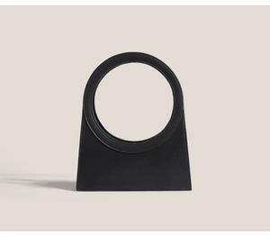 Detail of minimalist black handbag with unique large circular handle and trapezoidal shape