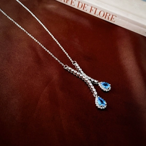 Détail du collier en Y argenté avec zircons goutte d'eau bleus sur tissu de soie