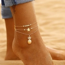 Three-layer gold anklet with pineapple and star charms worn on beach ankle