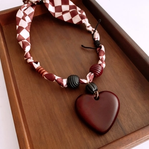 Close-up of heart pendant necklace with red plaid fabric cord and wooden beads