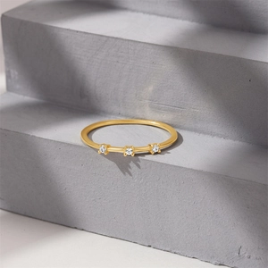 Macro shot of gold lace ring band featuring three sparkling zircons on a textured background