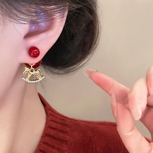 Gros plan d'une boucle d'oreille perle rouge avec pendentif cheval à bascule doré et zircons