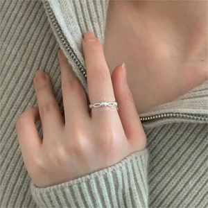 Detailed view of silver heart-shaped open ring worn against beige knitwear