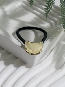 Detail view of a gold metallic spiral hair tie on a white textured pedestal