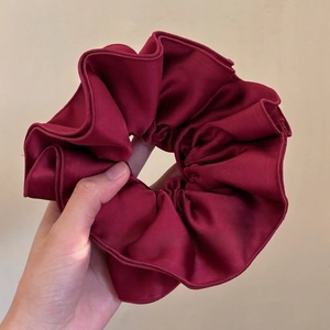 Close-up of a burgundy satin scrunchie with elegant wavy edges held in a hand