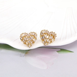 Gold hollow heart stud earrings with cubic zirconia set in a white ceramic dish