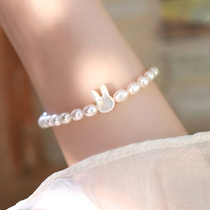 Close-up of a white pearl bracelet with a carved mother of pearl rabbit head on wrist