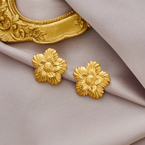 Détail de boucles d'oreilles fleur dorées à texture radiale sur fond de soie violette