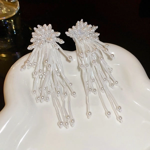 Detail of white beaded tassel earrings with flower pattern on a ceramic tray