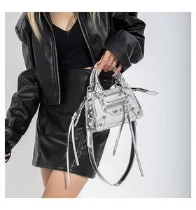 Detail of silver metallic handbag with rivets, fringe zippers and heart-shaped mirror