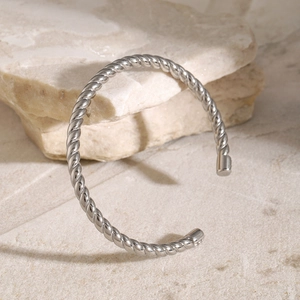 Detail of silver twisted rope cuff bracelet placed on a natural cream stone background