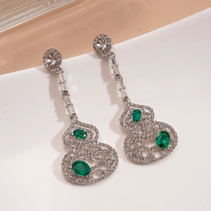 Élégantes boucles d'oreilles gourde argentées avec pierres vertes sur assiette blanche