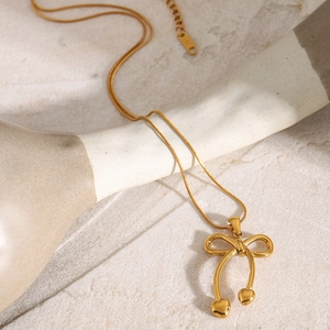 Detail shot of golden bow necklace with heart charms on light textured stone background