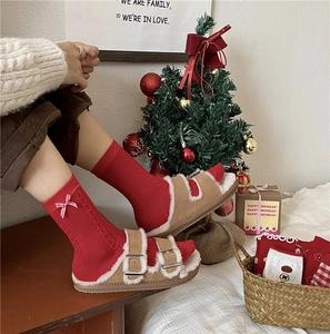 Cozy red Christmas socks with bows paired with warm brown plush sandals in a festive setting