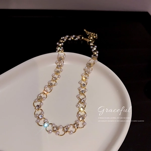 Détail d'un collier plaqué or avec des perles blanches et des cristaux brillants sur un plateau