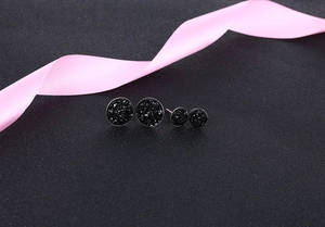 Macro detail of round black crystal stud earrings with silver base and matte texture