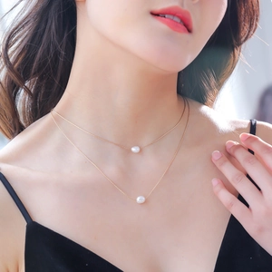 Double-layered gold necklace with two round white pearls worn by a model on plain background