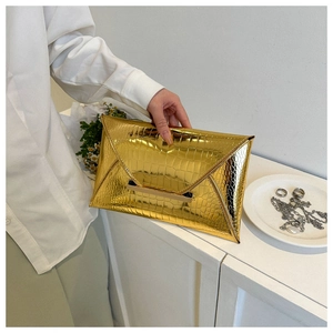 Detail of a gold crocodile pattern envelope clutch bag held in a hand for elegant evening look