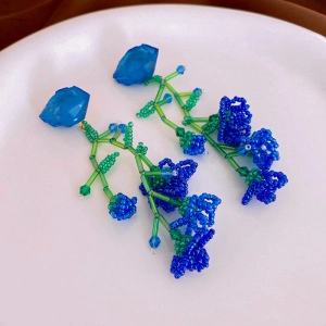 Detail of handmade blue beaded flower earrings with green leaf accents on white ceramic