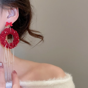 Close-up of red plush round earrings with a bow and elegant silver chain tassels