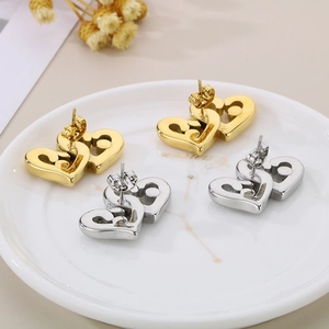 Detail of interlocking heart stud earrings in gold and silver on a ceramic tray