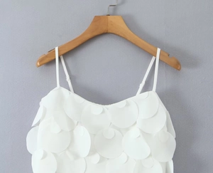 Dettaglio top bianco con paillettes e texture a petali stratificati su gruccia in legno