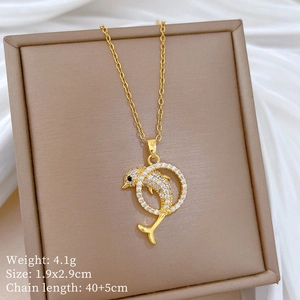 Detailed view of a gold dolphin necklace with cubic zirconia inlay in a beige jewelry box