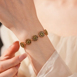Detail of a gold flower bracelet with green zircon petals on a model's wrist
