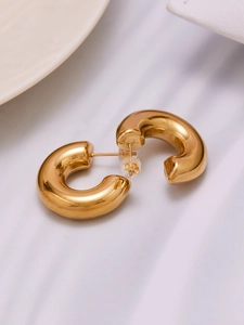 Detailed macro view of polished gold hollow C-shape hoop earrings on a white fabric background