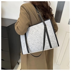 Close-up of a large grey quilted felt tote bag with black leather straps on a model