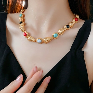Detail of vintage gold necklace with colorful inlaid gemstones on a black V-neck top