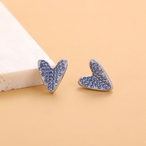 Macro shot of silver heart earrings with deep blue rhinestones on a stone surface