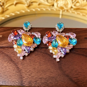 Close-up of heart-shaped earrings with colorful zircons on a vintage wooden base