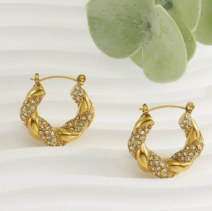 Detail view of gold twisted hoop earrings with micro-pave crystals on wavy background