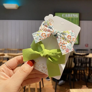 Close-up of green solid and floral bow hair clips held by hand on display card