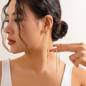 Elegant gold bow earrings with long tassels shown on model in a minimalist style