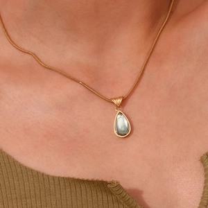 Detail of a vintage gold snake chain necklace with a translucent grey-green teardrop pendant