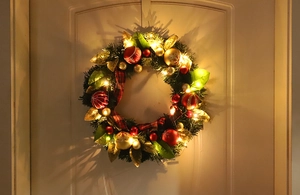 Close-up of lighted PVC Christmas wreath with red gold balls and plaid bow on white door