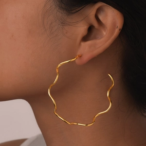 Detailed view of large wavy 18K gold-plated C-shaped hoop earrings on female model