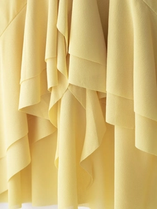 Macro shot of light yellow chiffon fabric showing fine texture and layered ruffle details