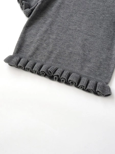 Detailed close-up of grey knit sweater featuring ruffled edges and fine ribbed texture
