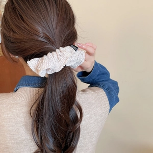 Detail of beige knitted scrunchie on low ponytail featuring vertical texture and fashion tag
