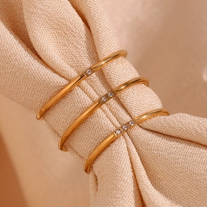 Three 18K gold plated titanium steel rings with micro-set crystals on beige fabric