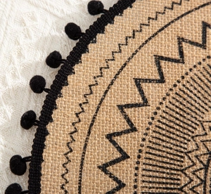 Detail of round woven jute placemat with black geometric stitching and fringe tassels
