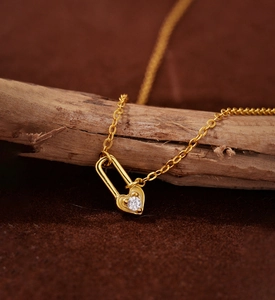 Close-up of golden heart lock necklace with white zircon stone draped on a branch