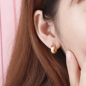 Close-up of golden zircon hoop earring worn by a model on a soft pink background
