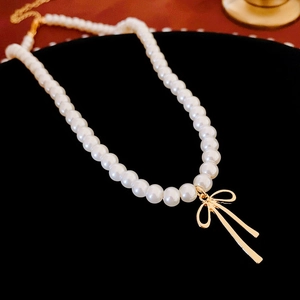 Close-up of pearl choker necklace with gold bow pendant on black velvet display