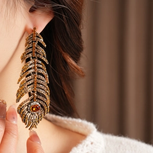 Close-up of vintage feather drop earrings with orange crystals on a model side profile